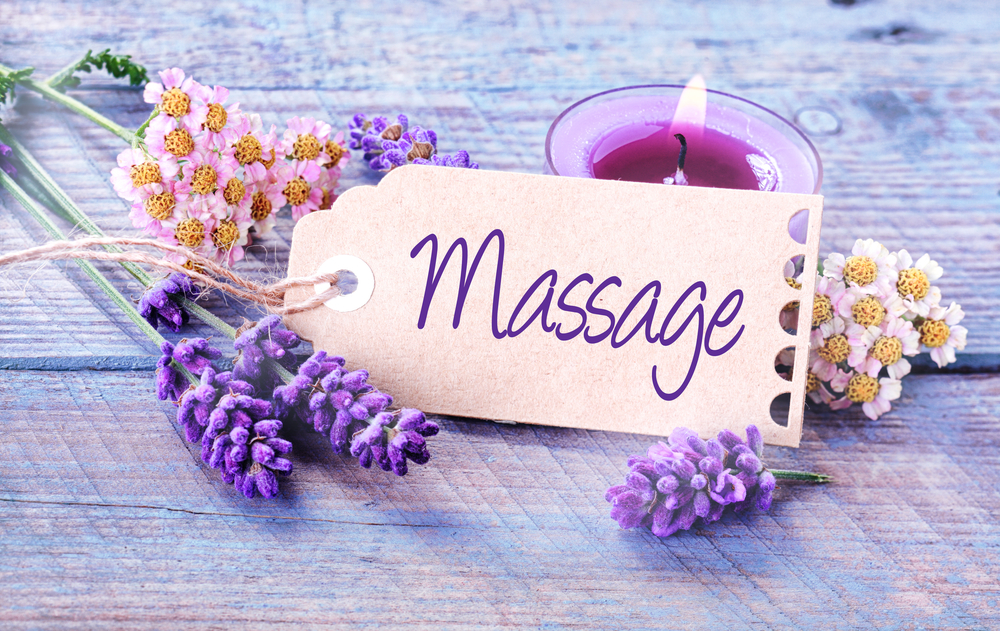 Massage kaartje ligt tussen lavendel en witte en roze bloemen met op de achtergrond een kaars.